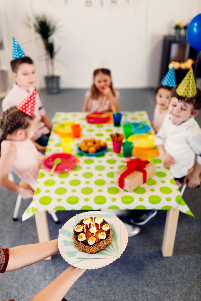 Djeca sa šarenim kapicama okupljena oko rođendanske torte
