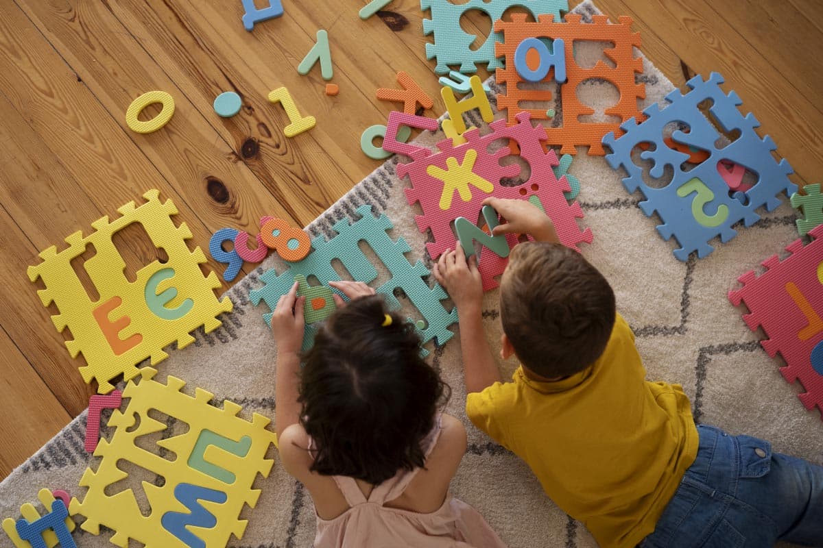 Dvoje djece slaže šarene pjenaste puzzle s brojevima i slovima na tepihu